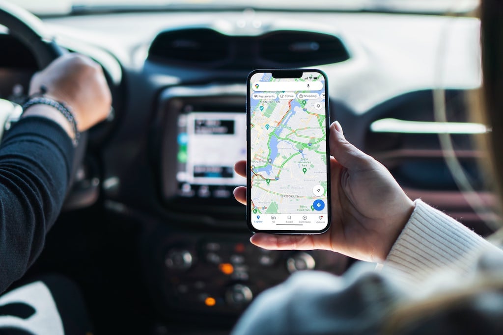 A passenger in a car holding a smartphone with a navigational map, showing a route.