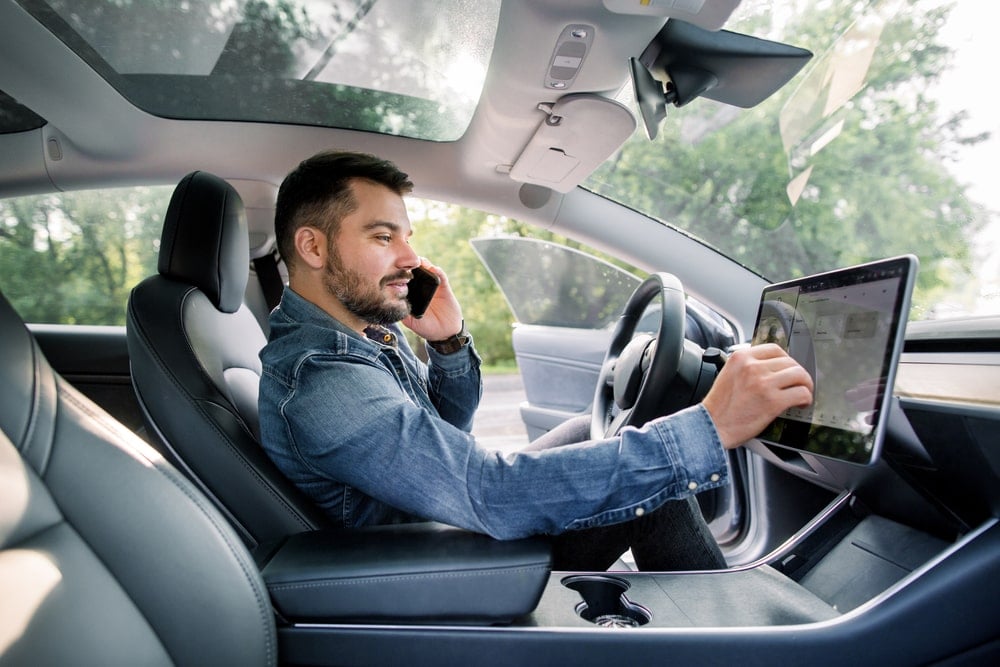 Modern man with beard in an electric vehicle, using his dashboard to navigate to his destination while on the phone.