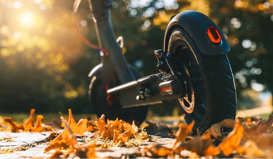 Elektrische step in herfstachtige omgeving met oranje blad op de grond