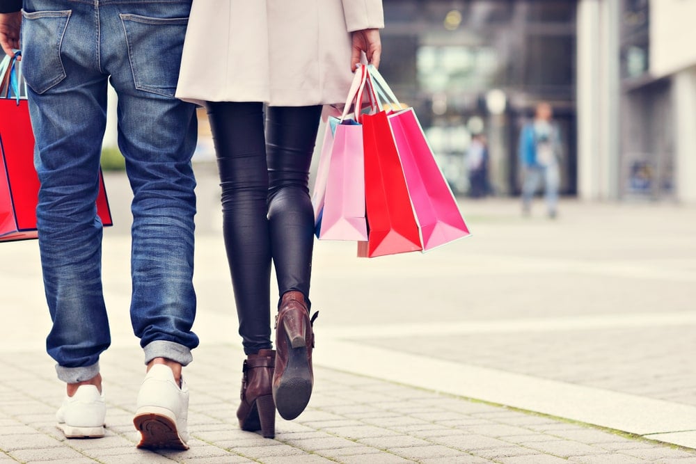 A close up shot of a fashionable couple holding shopping bags while walking in a city center.