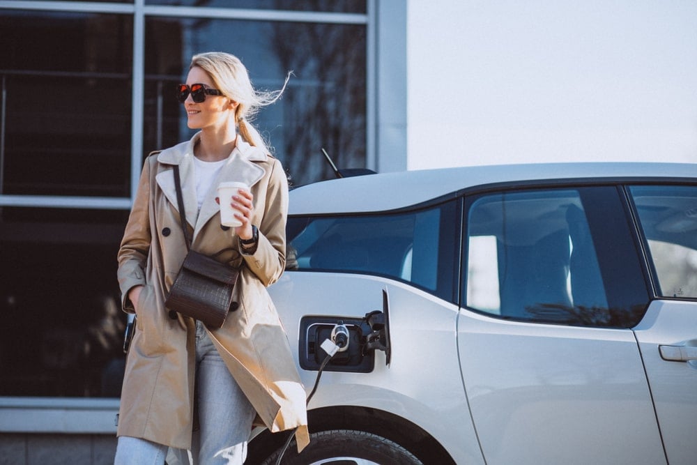 A woman holding a coffee while waiting for her EV being charged.