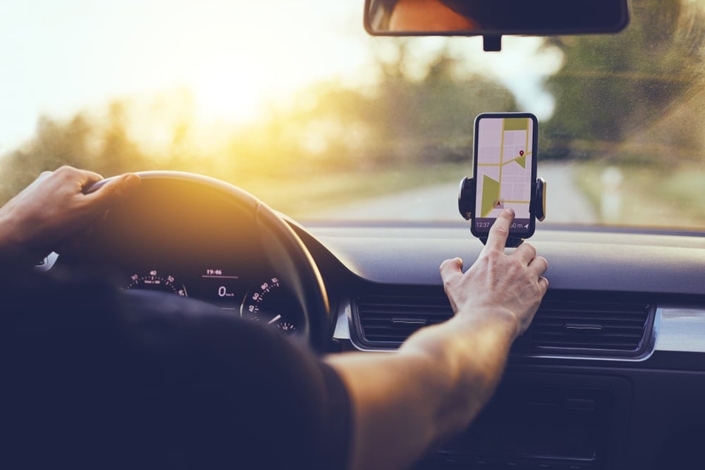 A man is checking his map on his smartphone while driving his EV to find a nearby fast charging station.