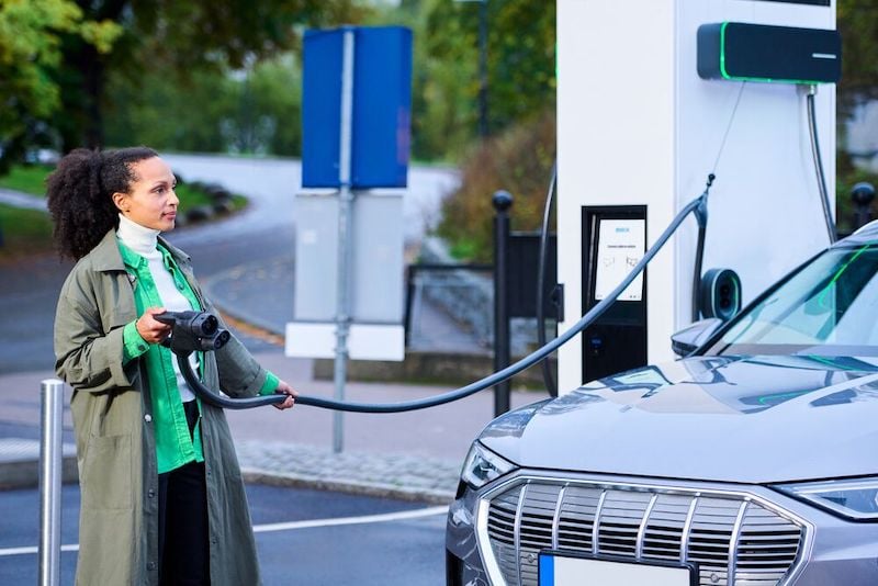 A woman is holding the charging cable that's connected to the cable management system of the  EVBox Troniq Modular.