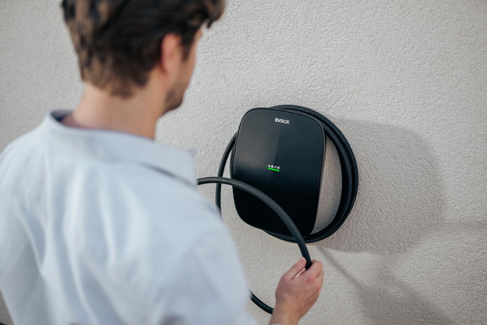 A man taking the cable from his mounted EVBox Livo AC charging station.