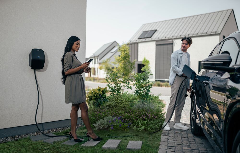 A man is charging his EV while a woman is checking her smartphone.