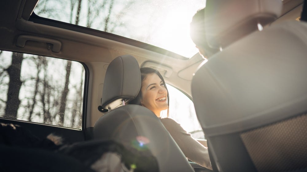 A woman is smiling while driving her EV on a sunny day.