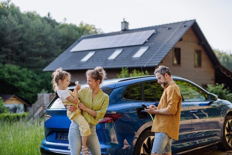 The dad is charging his EV with solar while the mom is playing with their kid.