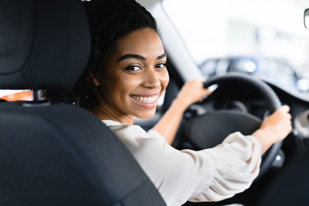 A woman who is driving her EV is smiling.