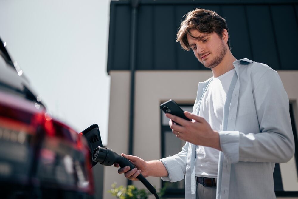 A man is charging his EV car while checking his phone.