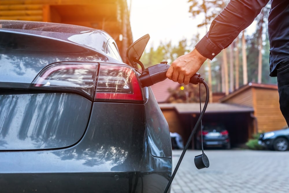 A man plugs a charging cable and charging plug into a dark grey EV.