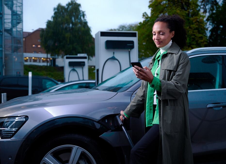 Woman charging her EV at an EVBox Troniq Modular charging station while looking at her phone and seeing real-time charging session information.