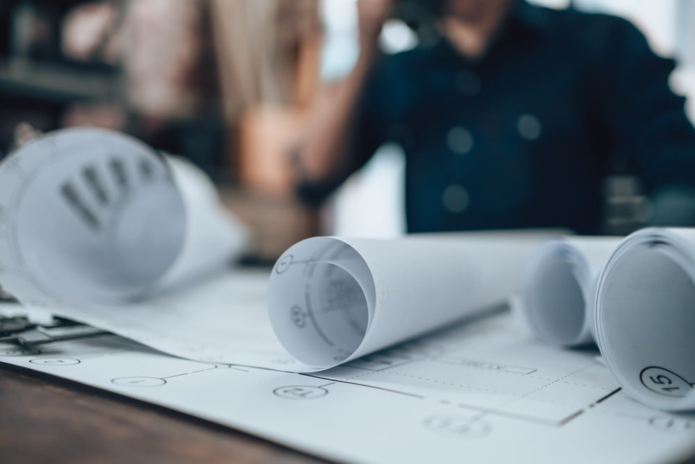 Engineering working with drawings rolled up on desks.