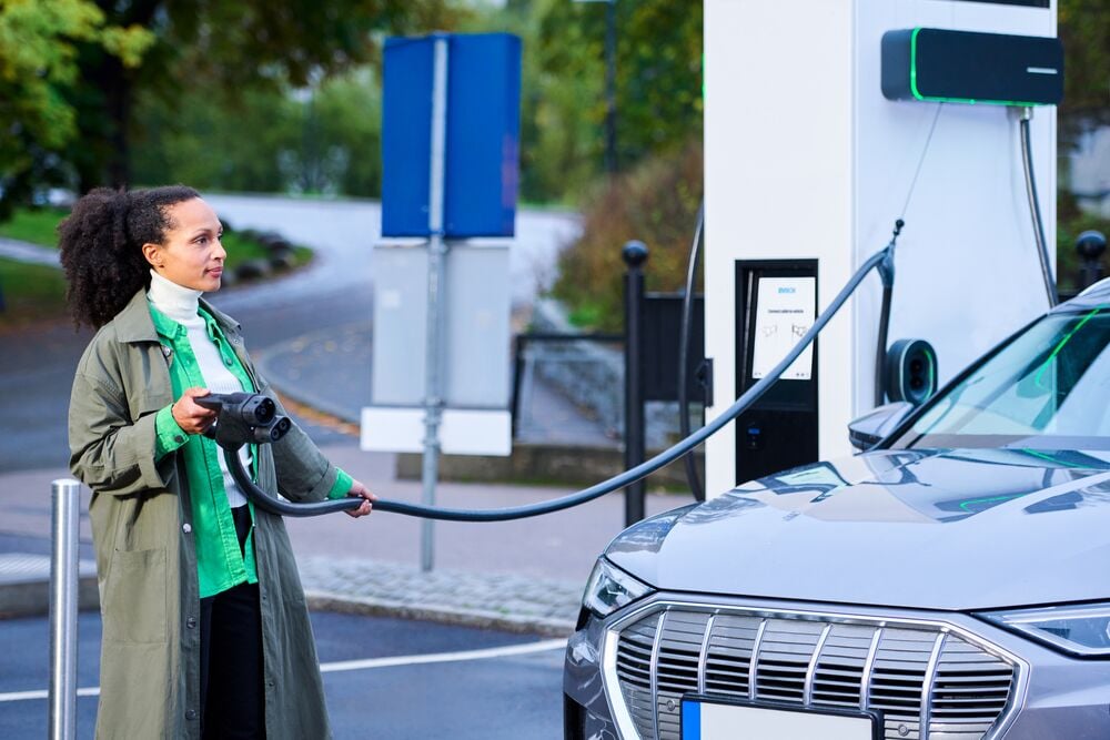 A lady in a raincoat holding a DC charging cable of the EVBox Troniq Modular.