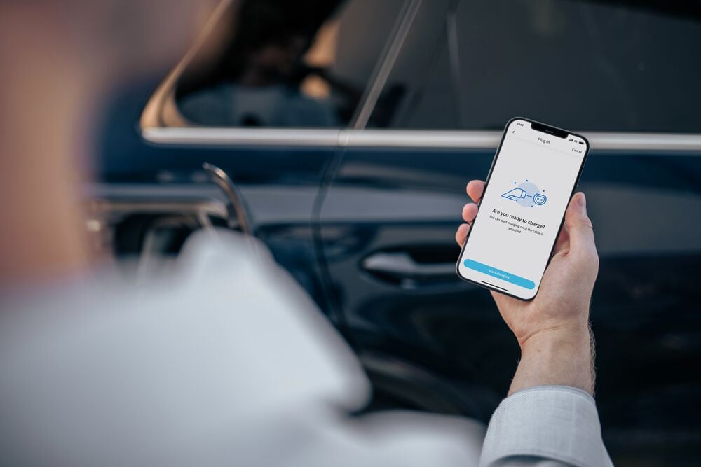 A man holding his smartphone to set up his safe and connected charging session via EVBox Everon software.