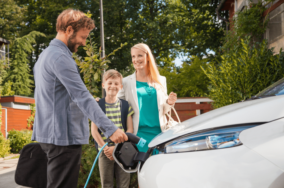 Man laadt elektrische auto op. Op de achtergrond staan een vrouw en een kind te glimlachen.