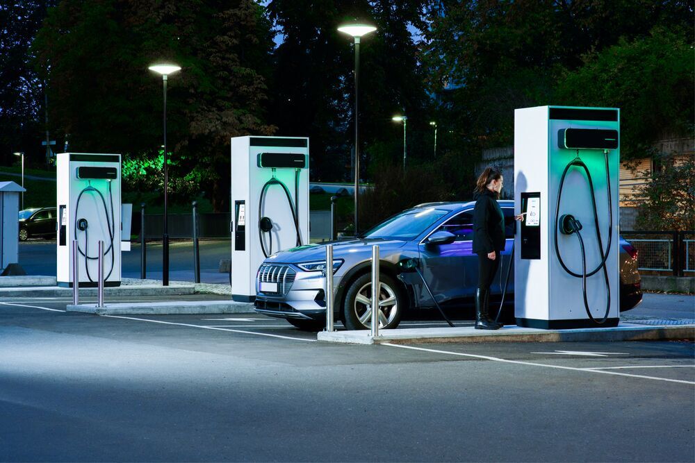 Une femme recharge sa voiture électrique à une station de recharge EVBox Troniq Modular. Deux autres stations se trouvent derrière elle.