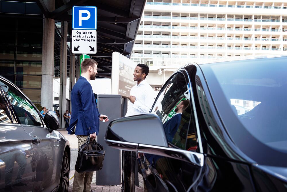 two guys talking to each other next to a public EV charging station.