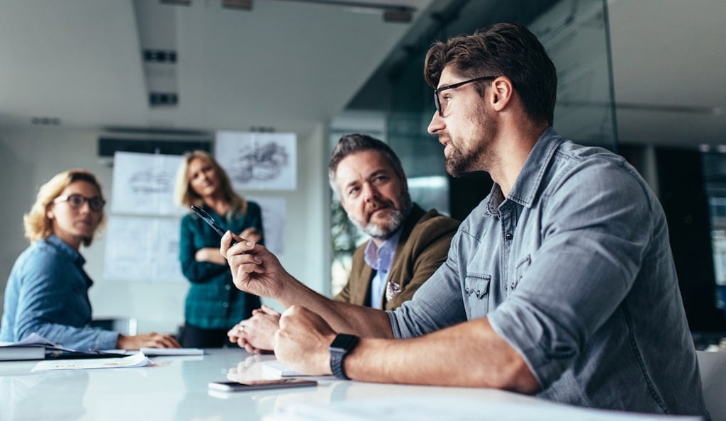 A business meeting where a young man wearing glasses explains the potential of commercial DC charging investment to his 3 colleagues.