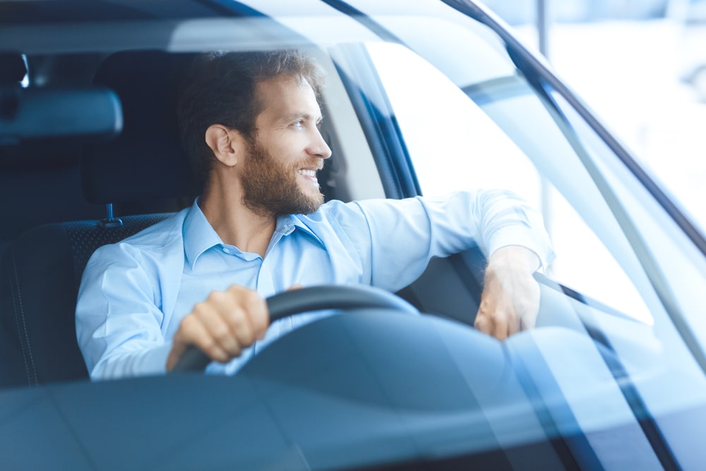 A man driving his EV rests his arm out of the car's open window.