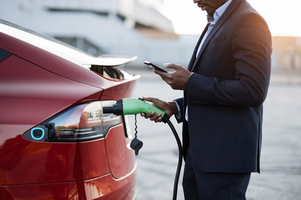 Man in suit holding charging cable for his electric car.