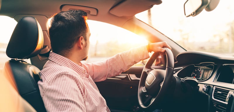 Side view of a driver sitting in comfortable new car with sunroof and looking out the window on sunset